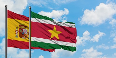 Spain and Suriname flag waving in the wind against white cloudy blue sky together. Diplomacy...
