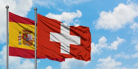 Spain and Switzerland flag waving in the wind against white cloudy blue sky together. Diplomacy...