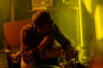 A young man, musician in glasses and a bathrobe sits in a chair and smokes a cigarette. Creative atmosphere. Cinematic style. Creative color