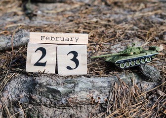 February 23. Holiday card with date of the 23th February on wooden calendar and model of toy tank. Men's day in Russia, Belarus, Tajikistan and Kyrgyzstan. Fatherland defender day. 