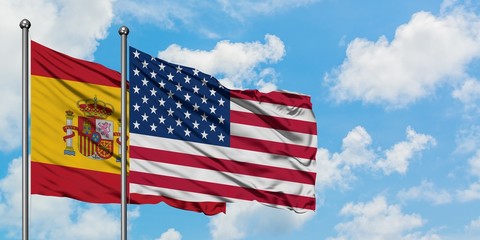 Spain and United States flag waving in the wind against white cloudy blue sky together. Diplomacy concept, international relations.
