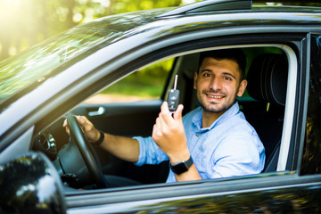 Young driver man sitting inside new car with keys. Smiling