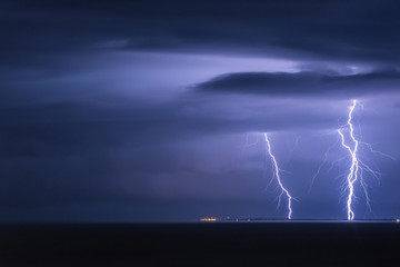 Massive cloud to ground lightning bolts hitting the horizon of city lights