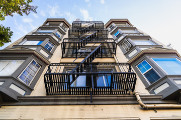 Exterior view of multifamily residential building; Old metal fire escape stairs hanging on side of the building; Berkeley, San Francisco Bay Area, California
