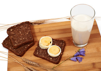 Slices of bread with eggs, glass of milk, rye and bluebell flower on cutting board