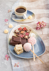 A pieces of homemade chocolate with coconut candies and a cup of coffee on a gray concrete background. side view.