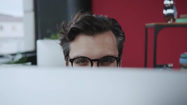Close-up funny tricky office manager showing eyes behind monitor flirting or spying working at desktop computer. Fun time. Office people.