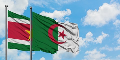 Suriname and Algeria flag waving in the wind against white cloudy blue sky together. Diplomacy...