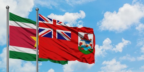 Suriname and Bermuda flag waving in the wind against white cloudy blue sky together. Diplomacy...