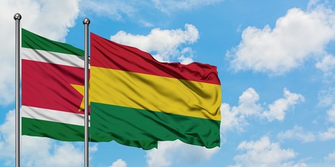 Suriname and Bolivia flag waving in the wind against white cloudy blue sky together. Diplomacy...