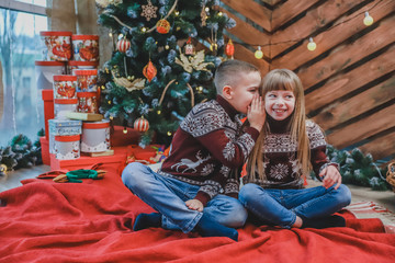 Cute brother whispering his sister something funny and shocking and she is looking amazed and curious.