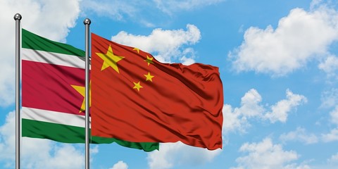 Suriname and China flag waving in the wind against white cloudy blue sky together. Diplomacy...