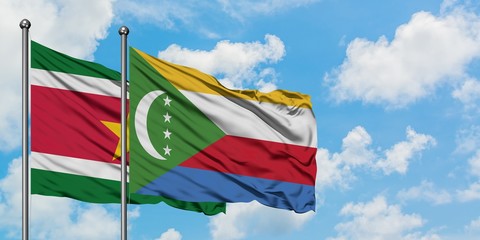 Suriname and Comoros flag waving in the wind against white cloudy blue sky together. Diplomacy concept, international relations.