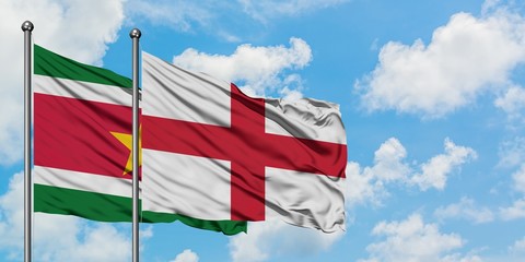 Suriname and England flag waving in the wind against white cloudy blue sky together. Diplomacy...