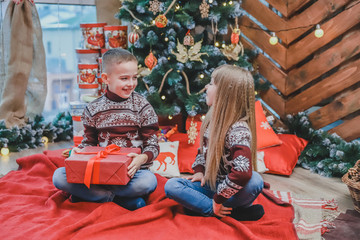 Two kids sharing christmas gift boxes sitting in christmas designed atmosphere.