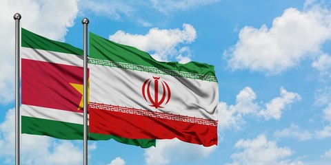 Suriname and Iran flag waving in the wind against white cloudy blue sky together. Diplomacy concept, international relations.