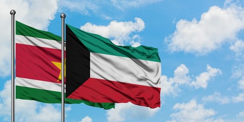 Suriname and Kuwait flag waving in the wind against white cloudy blue sky together. Diplomacy concept, international relations.