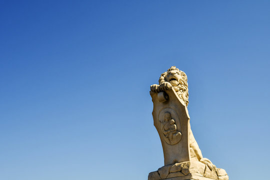Close-up of a marble statue of a lion holding a sign depicting Saint Mary with Baby Jesus, placed on one side of Solferino Bridge in Pisa, Tuscany, Italy