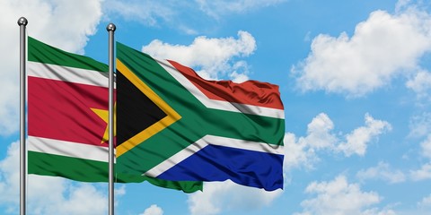 Suriname and South Africa flag waving in the wind against white cloudy blue sky together. Diplomacy...