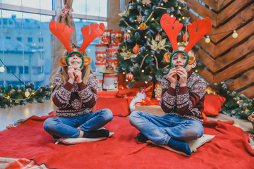 Cute little kids looking through reindeer antlers headgear, making fun on new year evening.