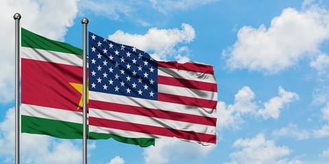 Suriname and United States flag waving in the wind against white cloudy blue sky together. Diplomacy concept, international relations.