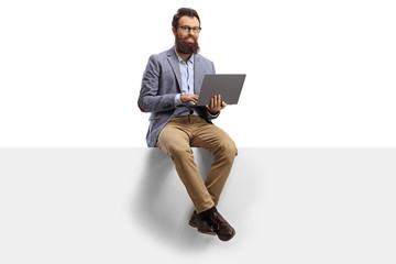 Bearded man working on a laptop and sitting on a banner