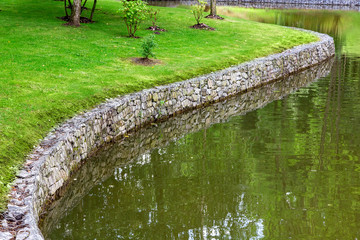 shore protection wall made of stone along the river, on the shore there is a lawn with green grass...