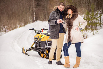 A young couple travels through the winter forest on snowmobiles.A man and a woman are watching geolocation on a smartphone.Snowmobile journey through the winter forest. People look at the phone screen
