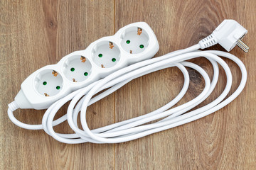 White four outlets power extension cord on a wooden surface. New electric power strip for home or...