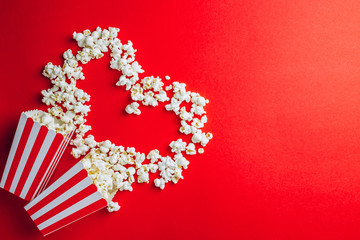 Tasty salted popcorn in striped cardboard box on red background. Top view. Flat lay. Copy space....