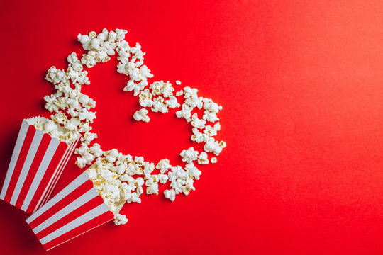 Tasty salted popcorn in striped cardboard box on red background. Top view. Flat lay. Copy space. Heart shape, Valentines day