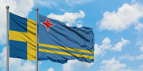 Sweden and Aruba flag waving in the wind against white cloudy blue sky together. Diplomacy concept, international relations.
