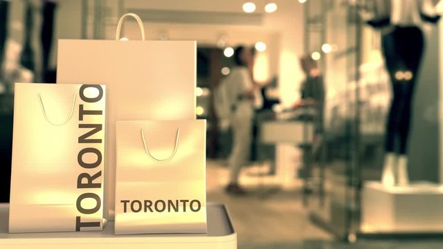 Paper shopping bags with TORONTO text against blurred store. Canadian shopping related clip