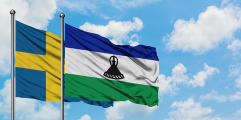 Sweden and Lesotho flag waving in the wind against white cloudy blue sky together. Diplomacy...