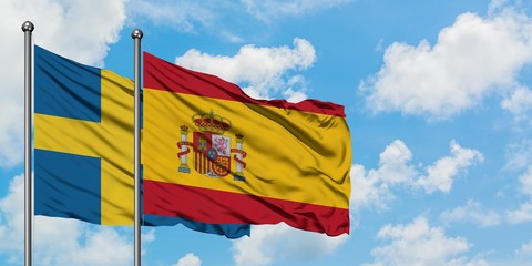 Sweden and Spain flag waving in the wind against white cloudy blue sky together. Diplomacy concept, international relations.