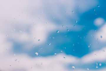 raindops on window glass with bokeh of serene blue sky with few clouds