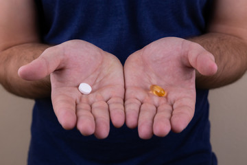 Man hands giving two big pills. White and orange. Make your selection. Health or ill. Choose your side.