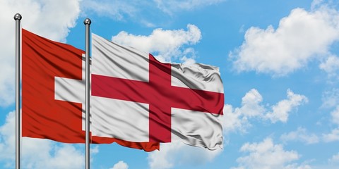 Switzerland and England flag waving in the wind against white cloudy blue sky together. Diplomacy concept, international relations.