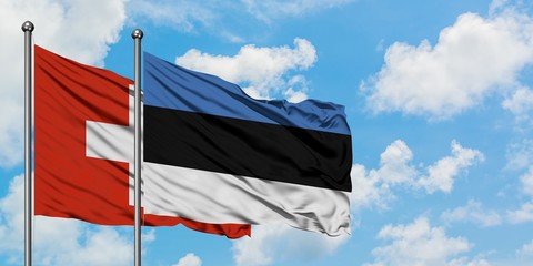 Switzerland and Estonia flag waving in the wind against white cloudy blue sky together. Diplomacy...