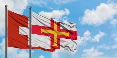 Switzerland and Guernsey flag waving in the wind against white cloudy blue sky together. Diplomacy concept, international relations.