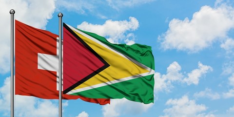 Switzerland and Guyana flag waving in the wind against white cloudy blue sky together. Diplomacy concept, international relations.