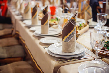 Beautifully folded napkins on a served table. Brown napkins on a white plate. Celebration in the restaurant. Cafe party at the banquet.