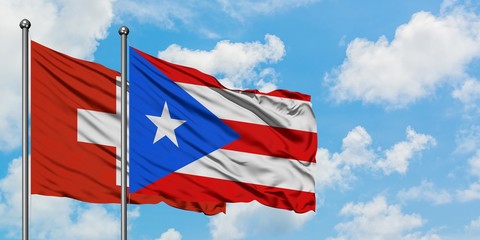 Switzerland and Puerto Rico flag waving in the wind against white cloudy blue sky together. Diplomacy concept, international relations.