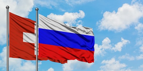 Switzerland and Russia flag waving in the wind against white cloudy blue sky together. Diplomacy concept, international relations.