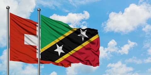 Switzerland and Saint Kitts And Nevis flag waving in the wind against white cloudy blue sky together. Diplomacy concept, international relations.