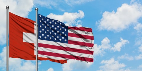 Switzerland and United States flag waving in the wind against white cloudy blue sky together. Diplomacy concept, international relations.