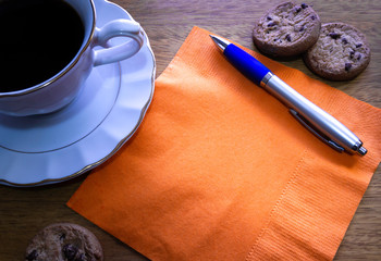 Taza de café con galletas, servilleta y bolígrafo sobre una mesa