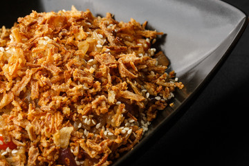 Asian fried rice with eggs, tomatoes, chilli, fried onion and sesame close-up on a plate, horizontal view from above. Nigerian food party: Jollof rice with fried onion close-up on a plate.
