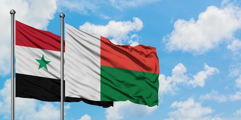 Syria and Madagascar flag waving in the wind against white cloudy blue sky together. Diplomacy...
