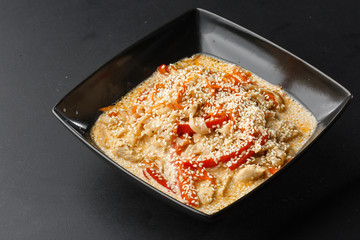  hicken with vegetables and udon noodles in a delicate creamy cheese sauce in a black bowl on a black background. Horizontal photo.